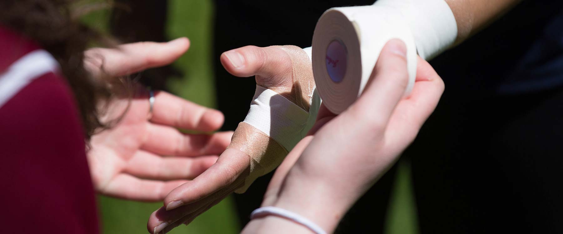 An athletic training student uses tape to wrap an athletes wrist and hand.