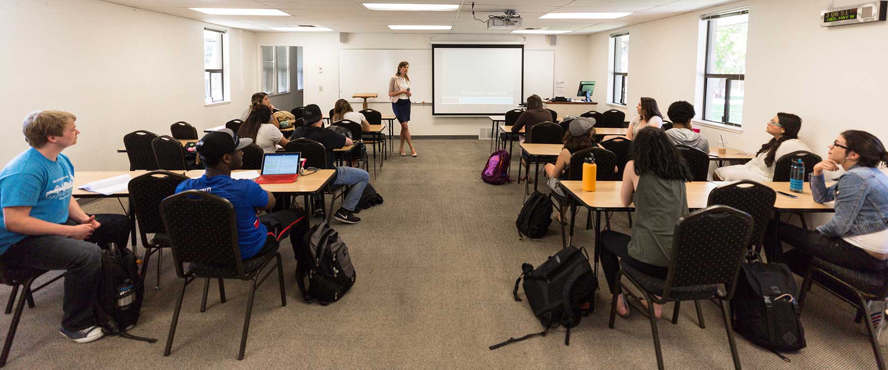 A professor stands at the front of a classroom speaking to the students.