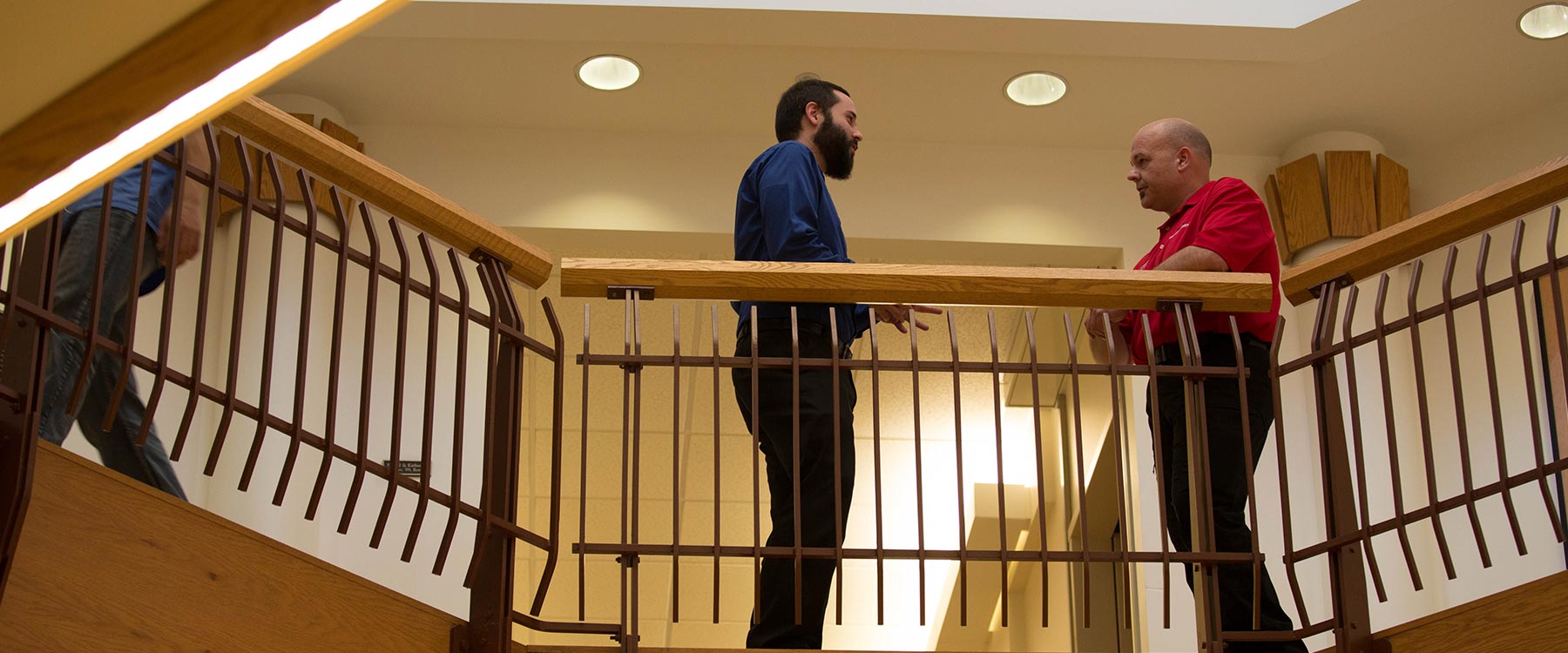 A continuing studies student stands talking with his professor near a balcony railing.
