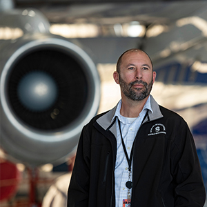 Jeff Mitchell stands in front of an airplane.