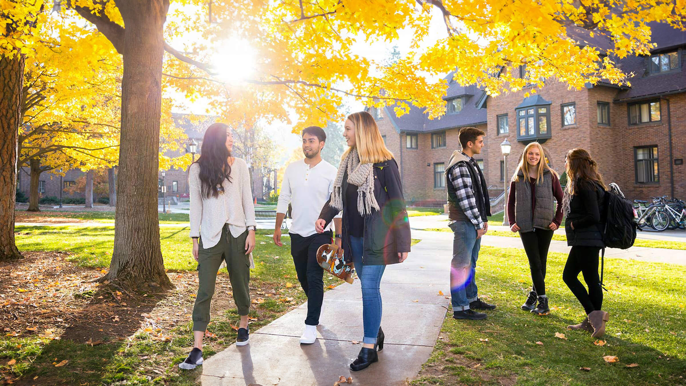 Students walk on campus, with a tree in fall colors behind them.