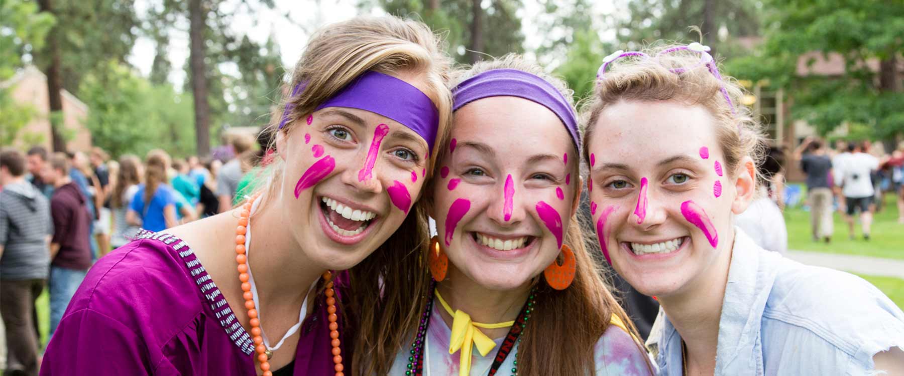 Three students, with headbands and bright face pain, stand close together and smile.