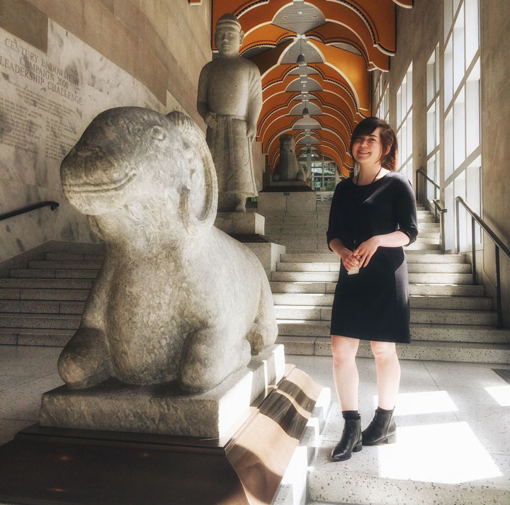 Portrait of Hannah Hirano on the interior steps of a museum with ancient-looking stone structures.