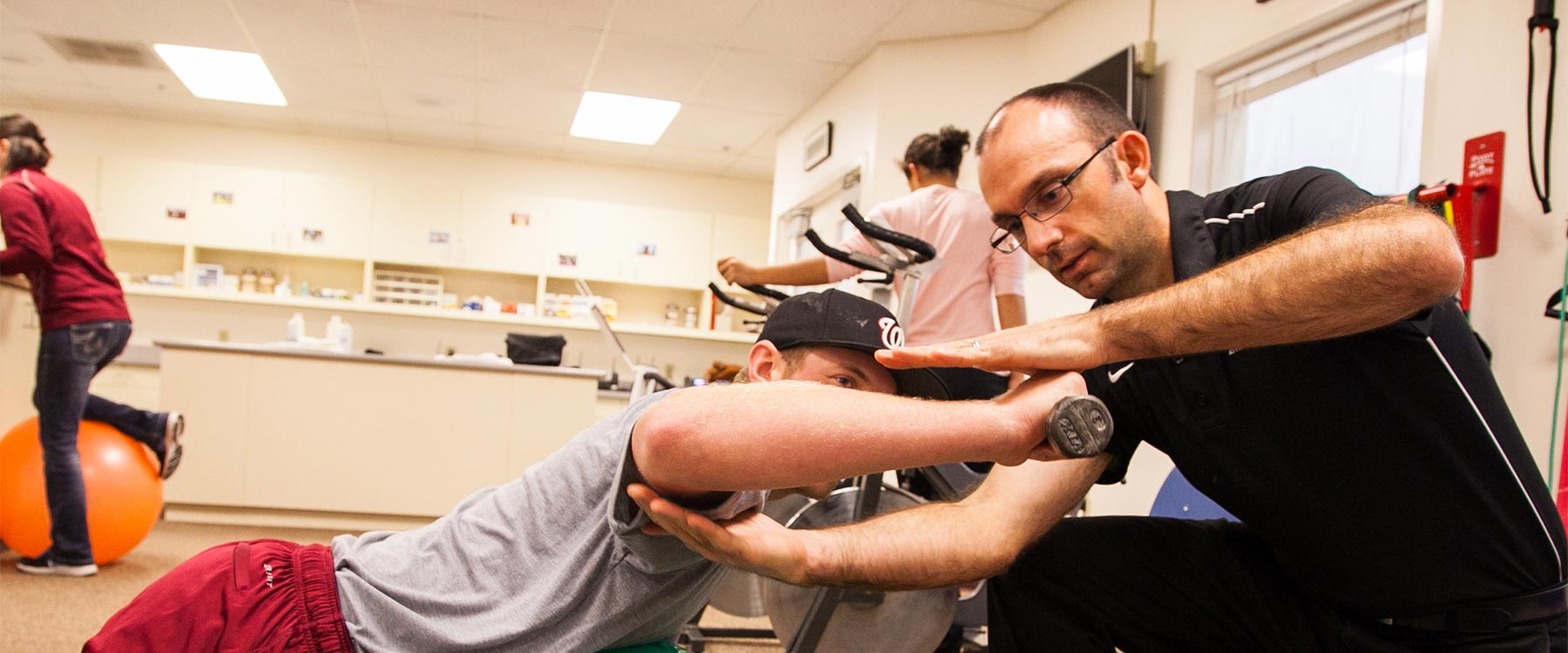 A professor helps an athletic training student with alignment as they lift a dumbbell.