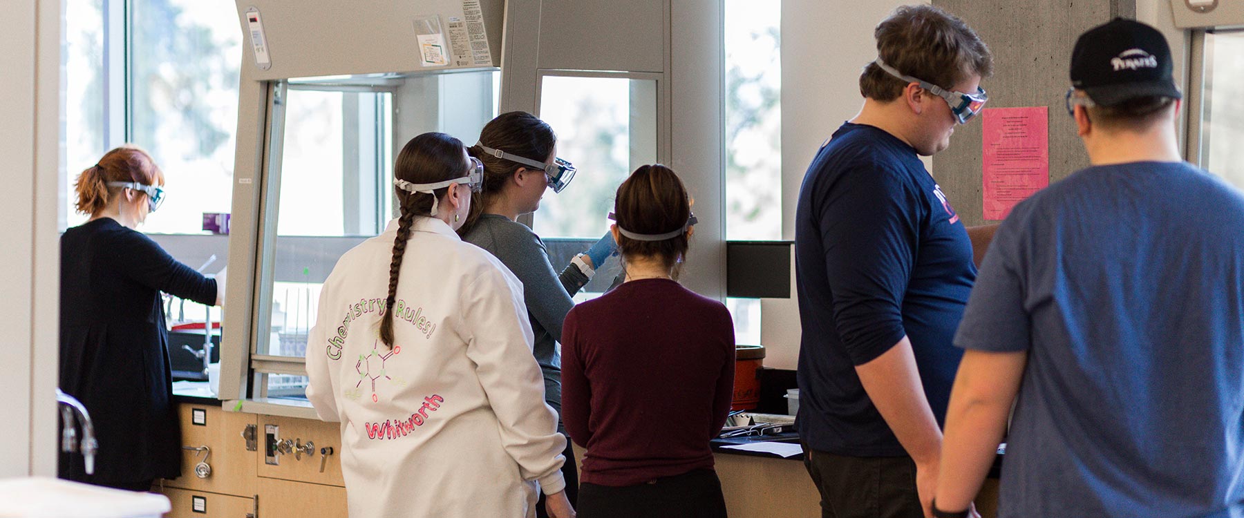 Students wearing lab coats and safety goggles conducting experiments in a science lab.