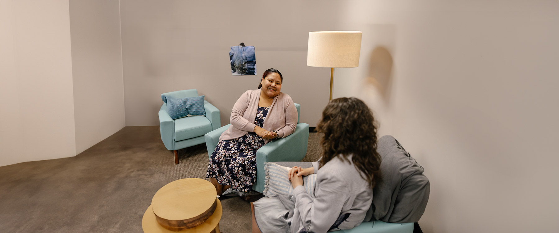 Two adults sit in small arm chairs, smiling and conversing with one another.
