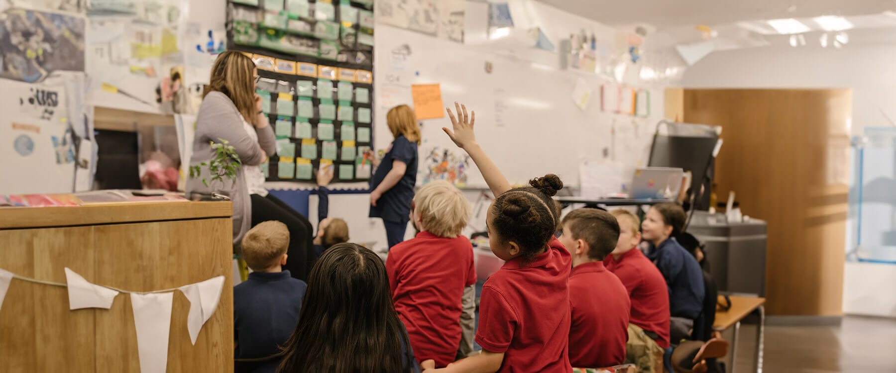 A teacher sits across from a middle school student in a classroom. They examine a globe closely.