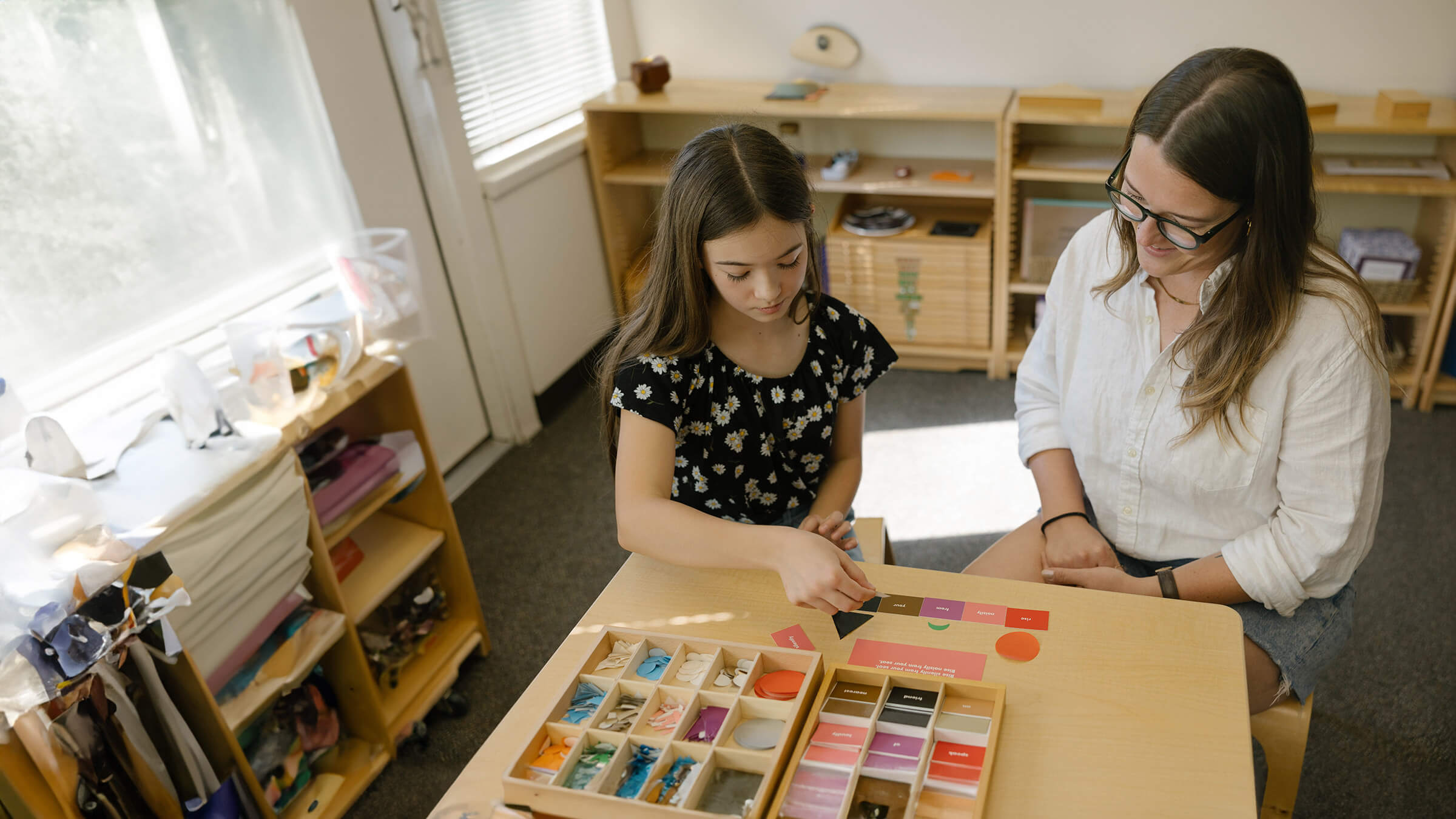 An elementary student learns language structure with colorful cards while a teacher assists.