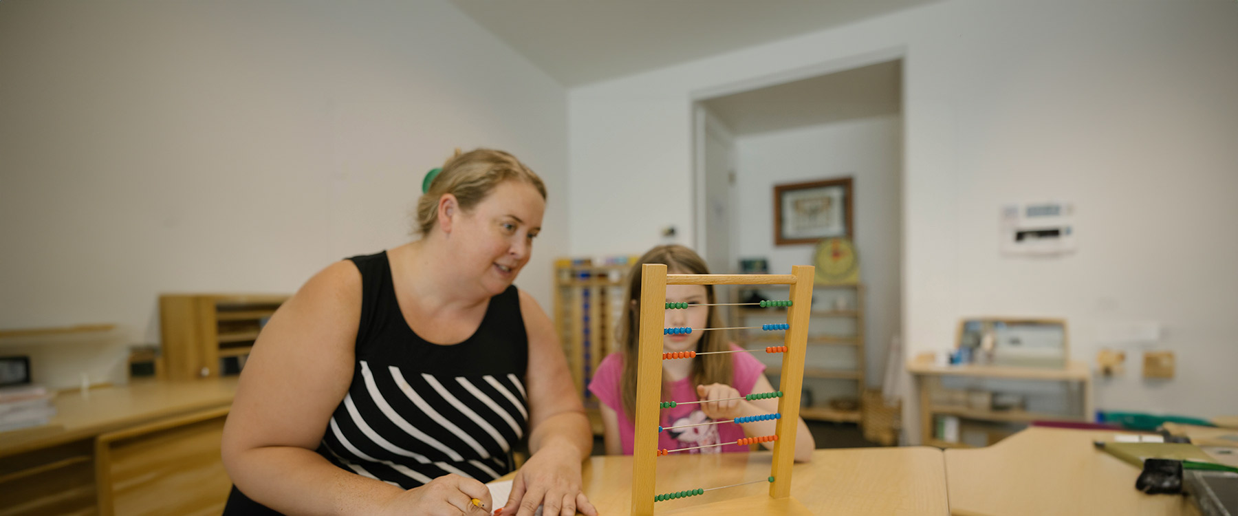 A teacher and elementary student sit in a classroom and practice calculations on an abacus.