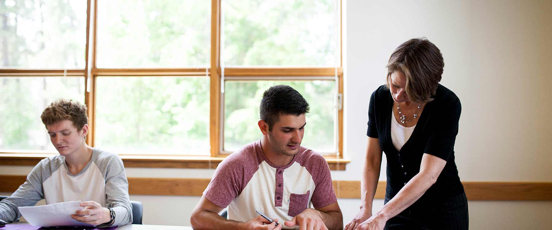 A professor stands next to a seated student. She points at something on his paper.