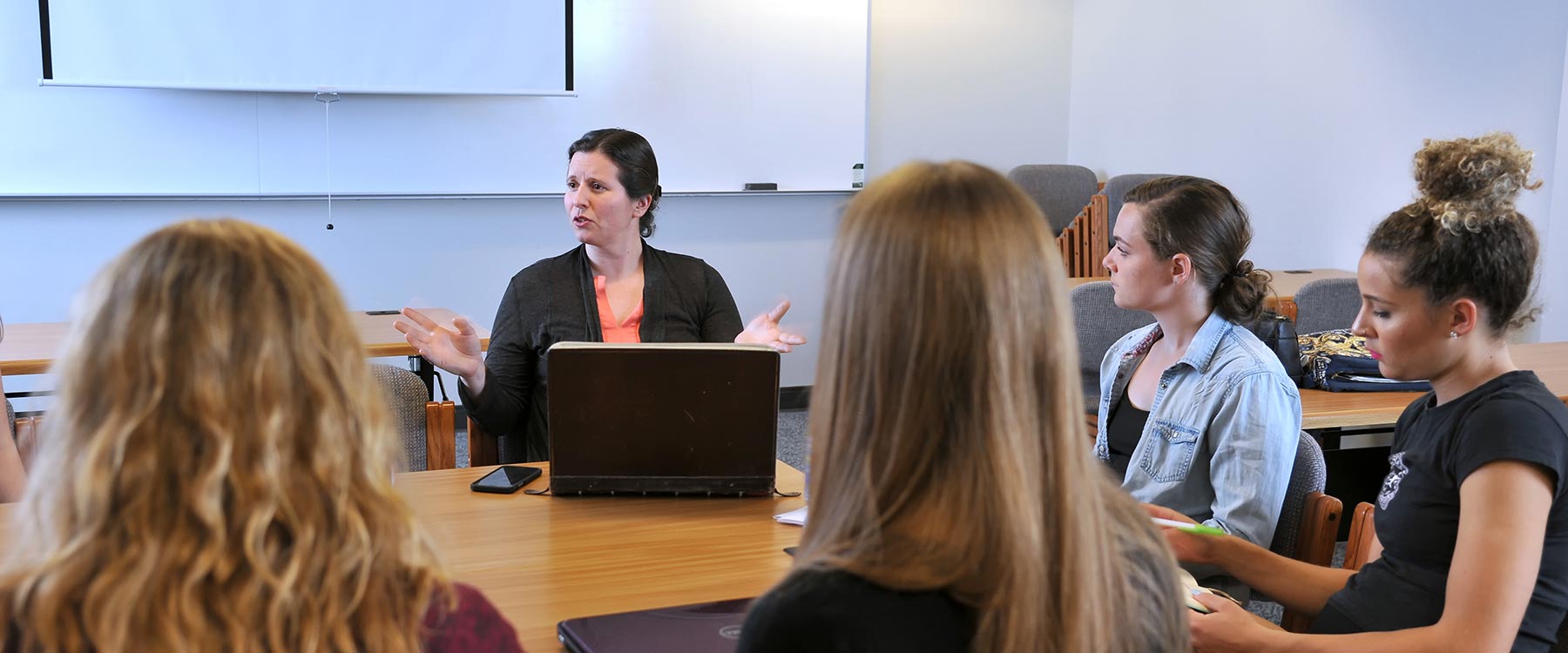 Professor Erica Salkin sits at a small table with a group of communication studies students, speaking with them.
