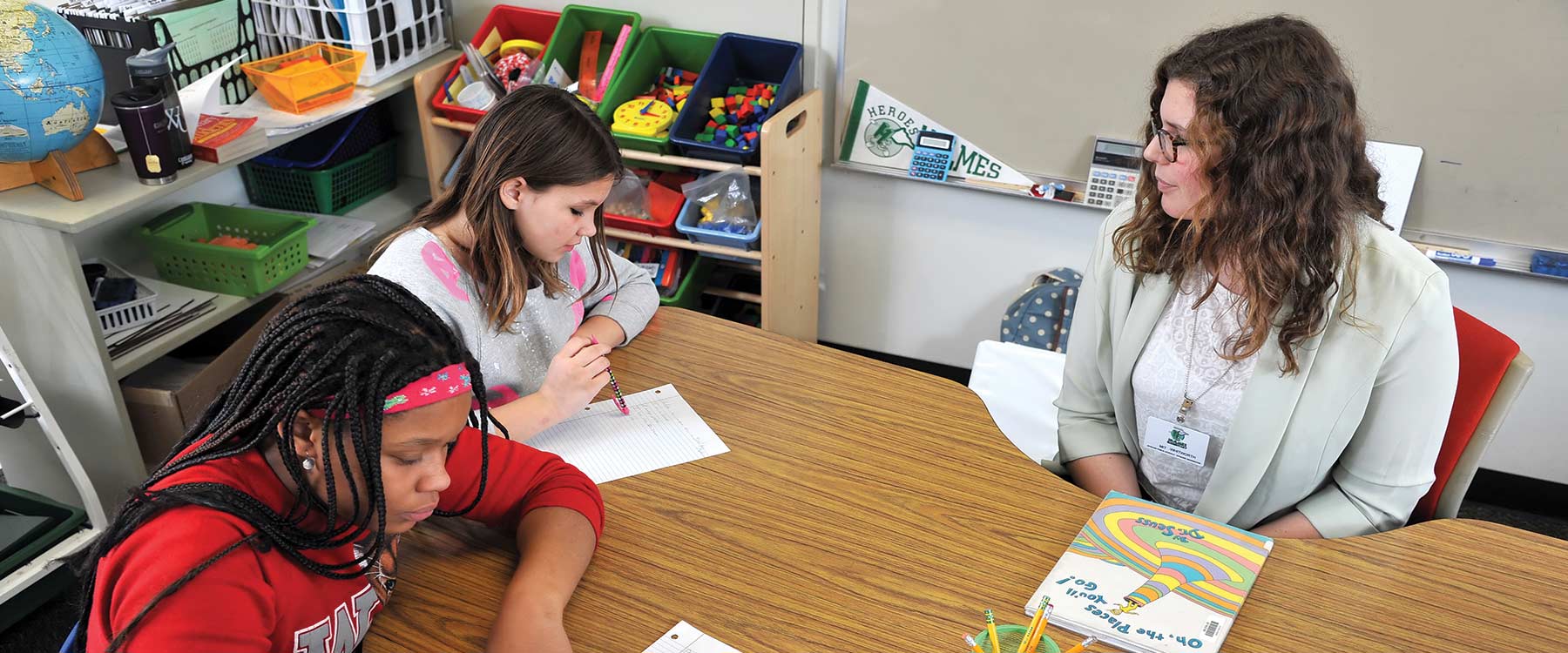 A future educator sits at a semicircle table with two middle school students as they work on a writing prompt.