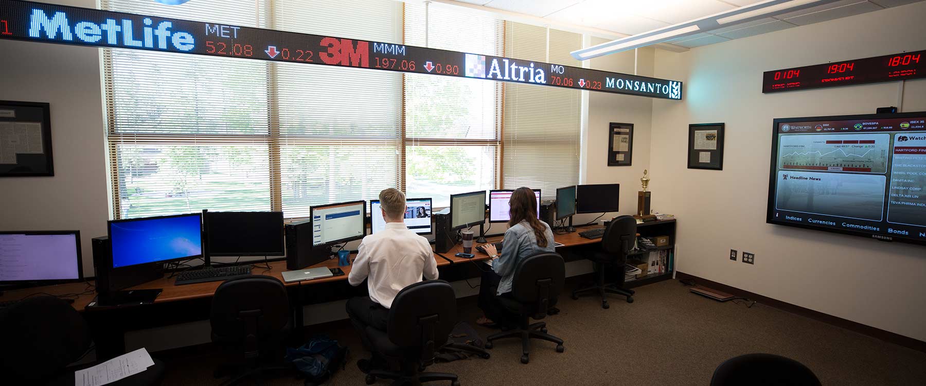 Students work on computers in the Whitworth Finance room. Above them a stock price ticker displays stock changes. 