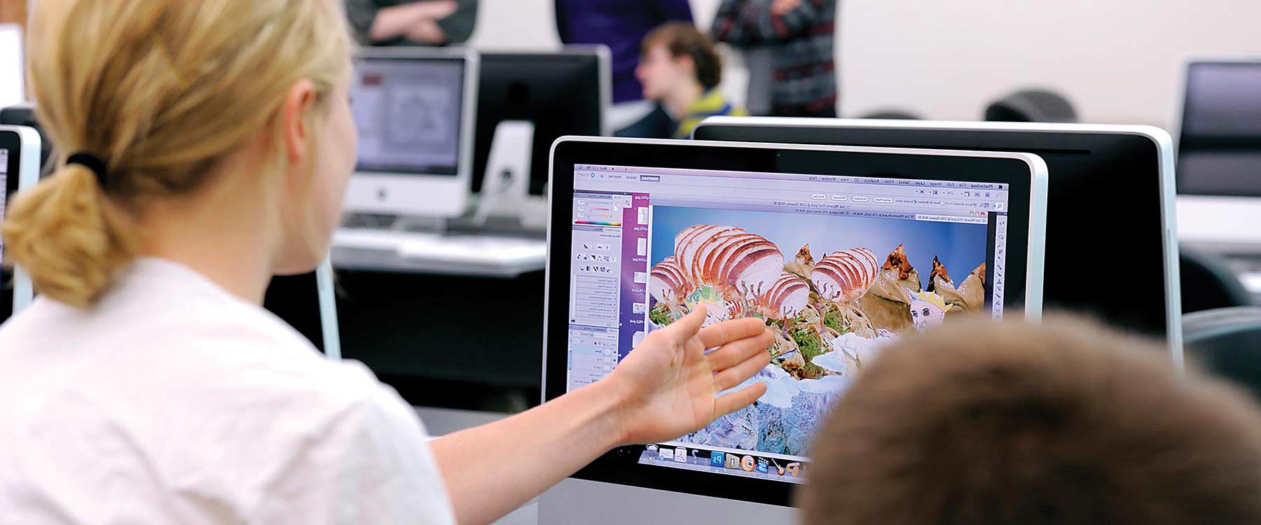 A student points to an iMac screen. On the screen is an eclectic and colorful design.