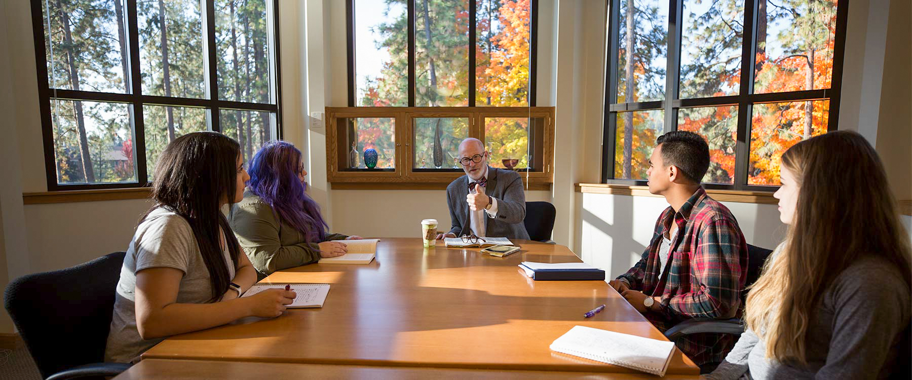 Professor Tony Clark sits at the end of a long table with students on either side listening intently.