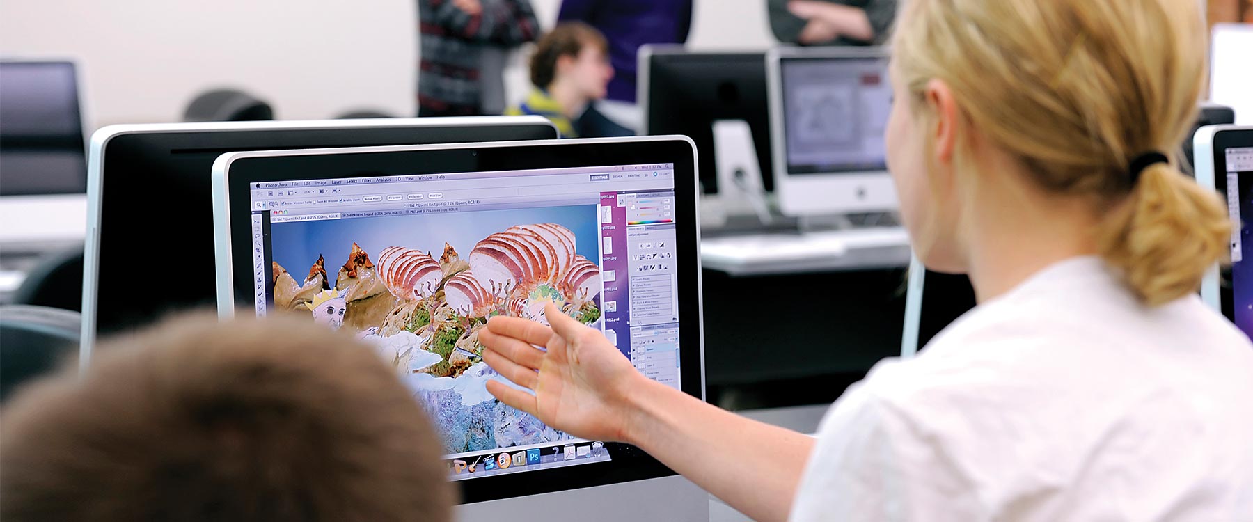 A student points to an iMac screen. On the screen is an eclectic and colorful design. 