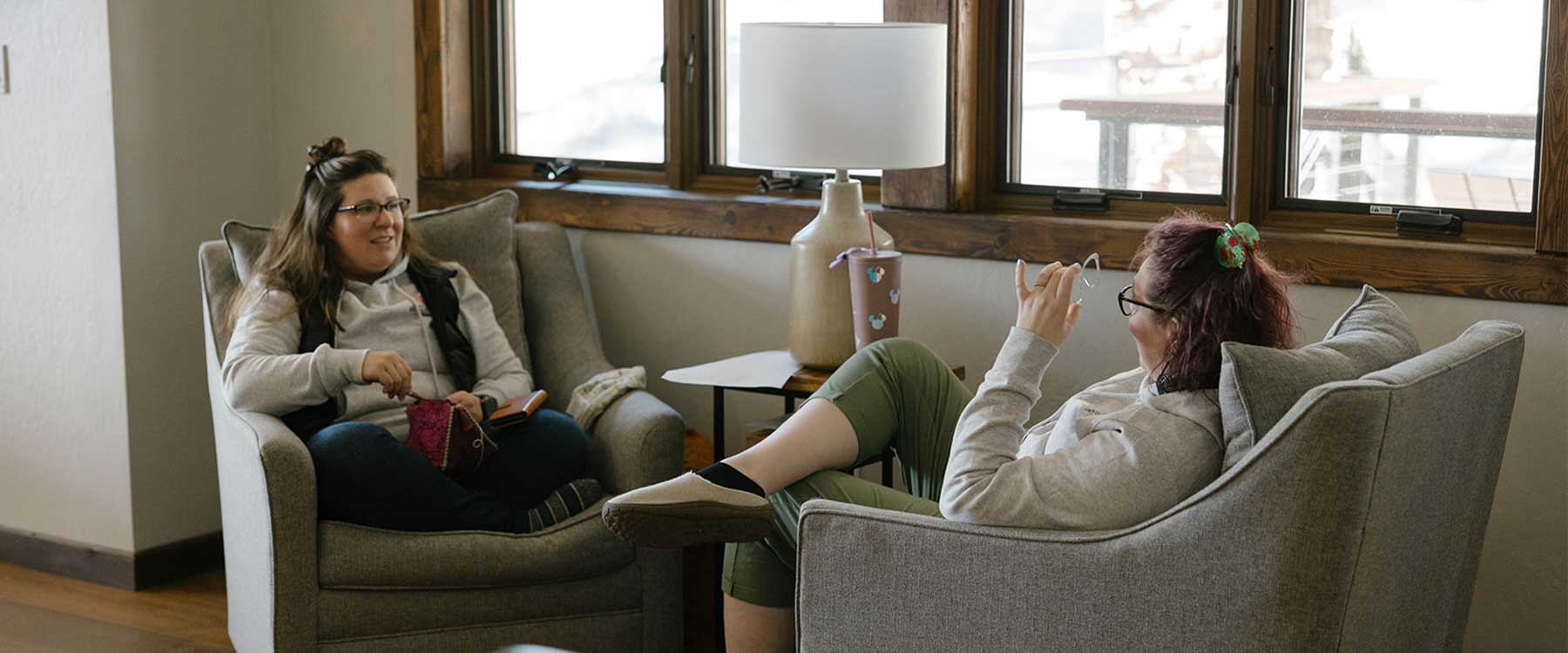 Two adults sit in small arm chairs, smiling and conversing with one another.