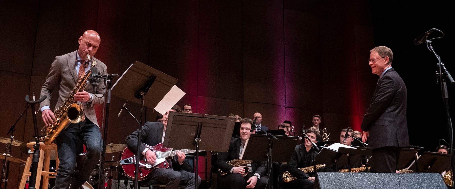 Joshua Redman performing with students and band director smiling, wide-eyed.