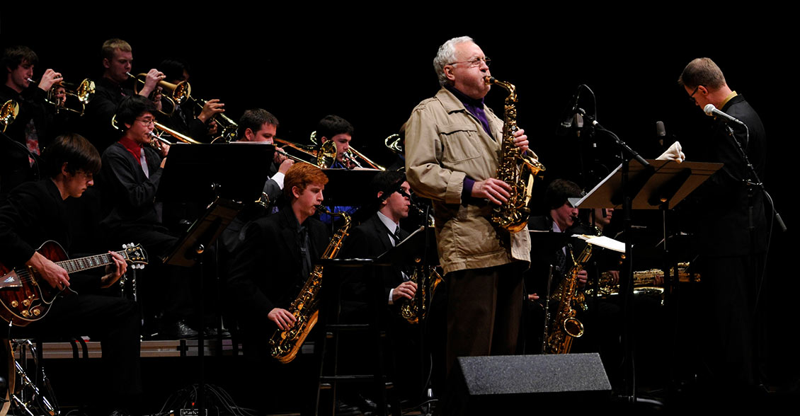 Lee Konitz playing saxophone in front of student instrumentalists.