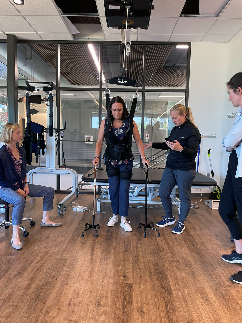 A student and instructor assist as a patient practices walking with the bioness vector elite system harness.