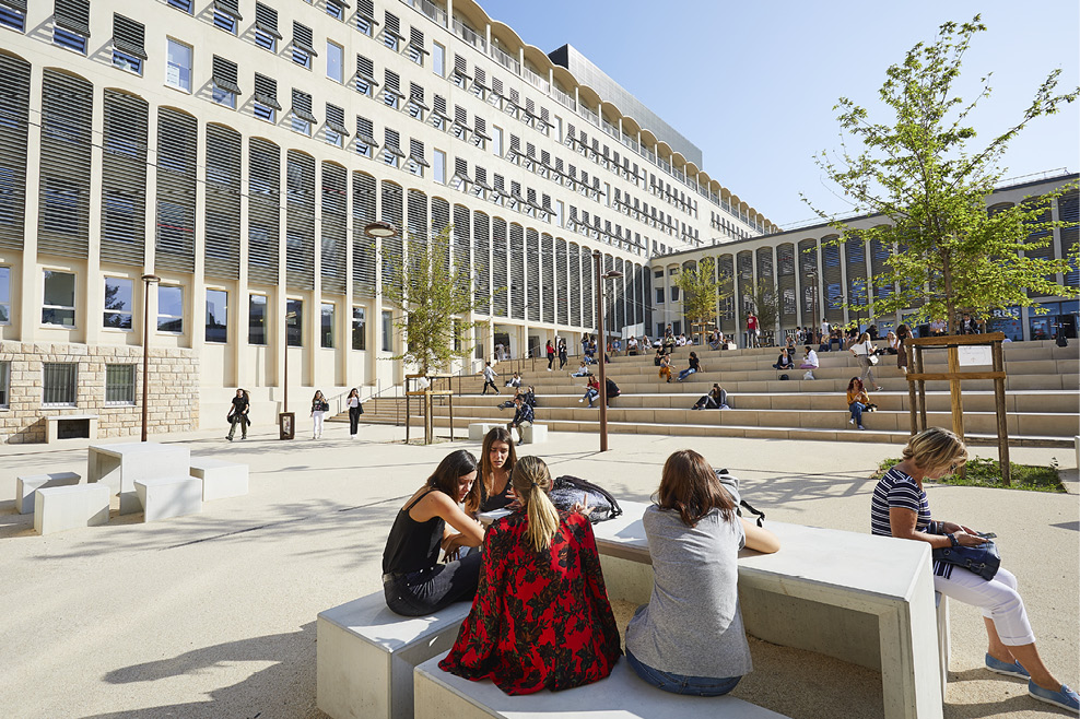A seven-story building and large outdoor courtyard with students sitting on benches and steps.