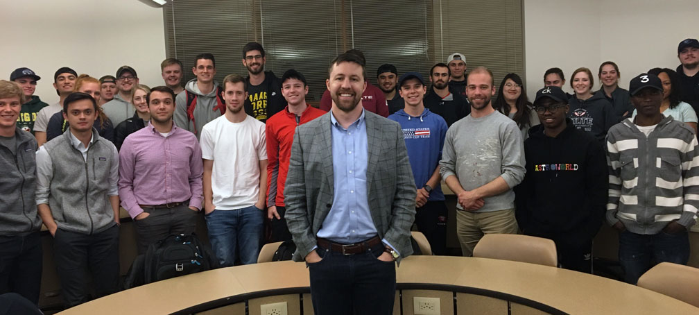 Aaron Vaccaro stands and smiles with a group of Whitworth business students.