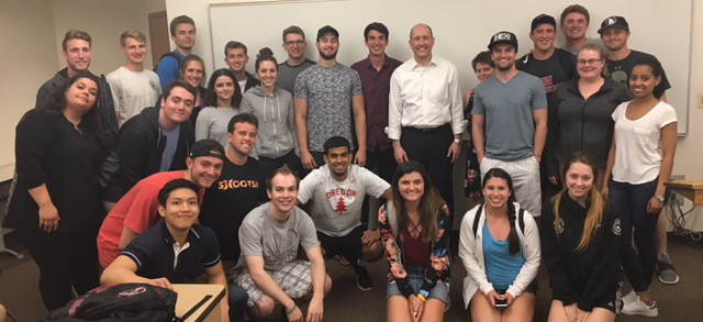 Beck Taylor and students pose, smiling, in front of a whiteboard in a classroom setting.