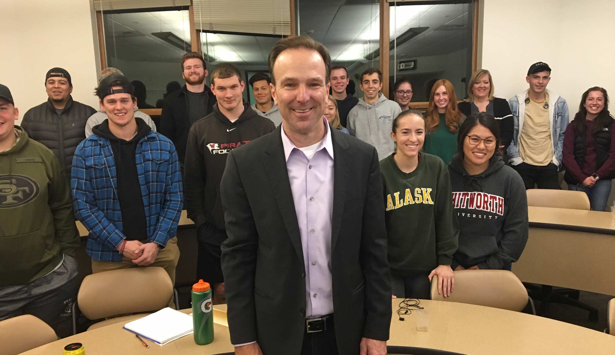 Bruce Bethards and students pose, smiling, around a semicircle desk.