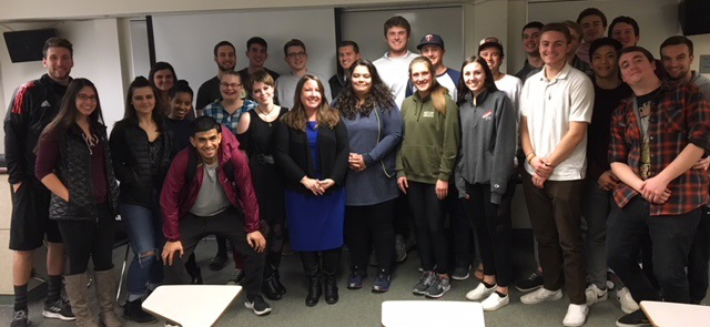 Carolyn Kadyk and students pose, smiling, in front of a whiteboard in a classroom setting.