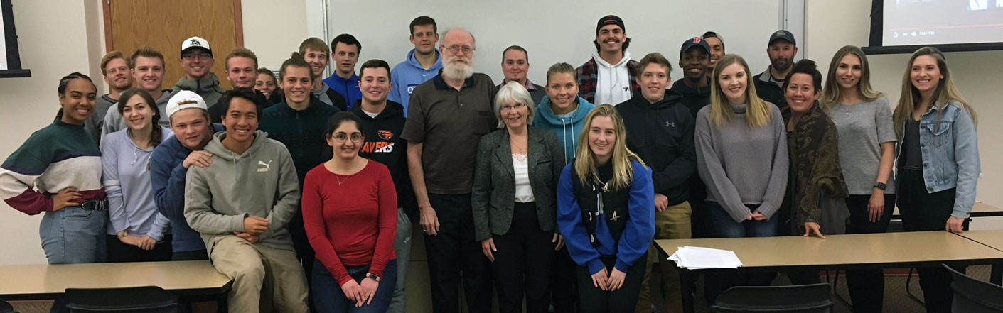 Christopher Burkett and students pose, smiling, in front of a whiteboard in a classroom setting.