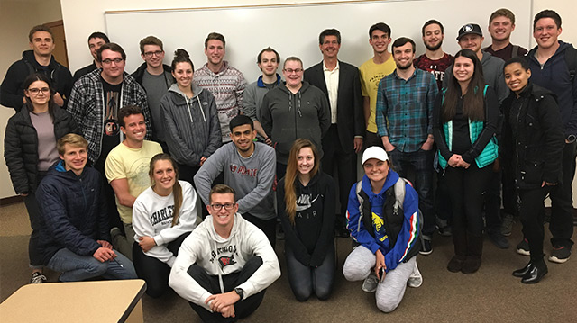 Dave Rogers and students pose, smiling, in front of a whiteboard in a classroom setting.