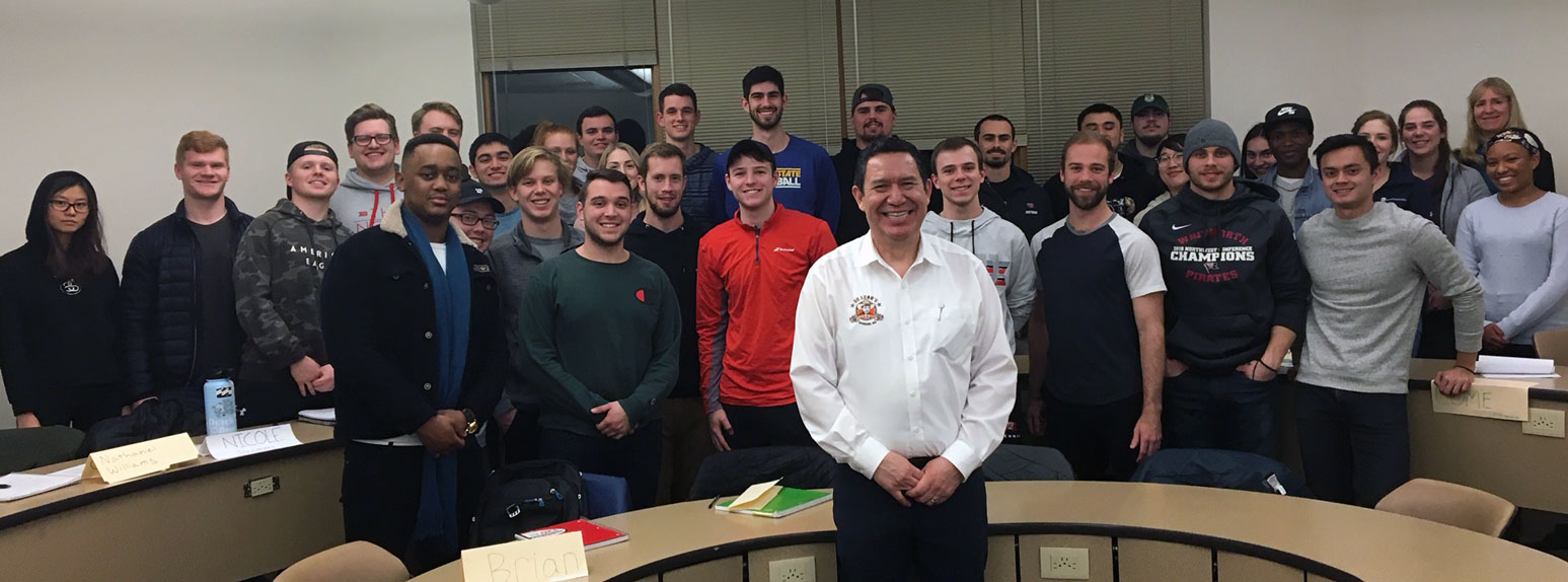 Sergio DeLeon and students pose, smiling, around a semicircle desk.