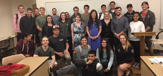 Erin Lyndon and students pose, smiling, in front of a whiteboard in a classroom setting.