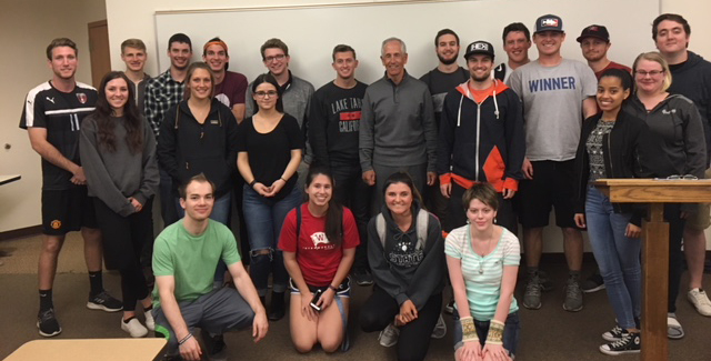 Fred Stockton and students pose, smiling, in front of a whiteboard in a classroom setting.