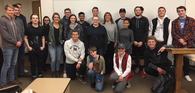 Kristin Goff and students pose, smiling, in front of a whiteboard in a classroom setting.