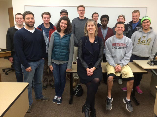 Holly Montgomery and students pose, smiling, in front of a whiteboard in a classroom setting.