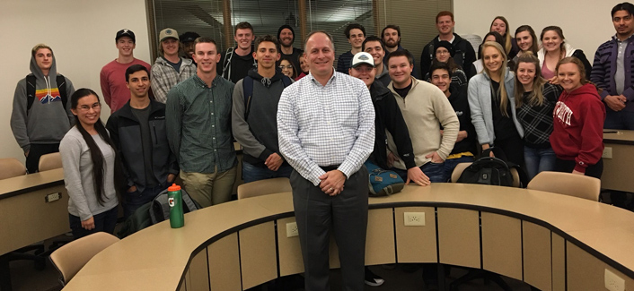 Jason Thackston and students pose, smiling, around a semicircle desk.