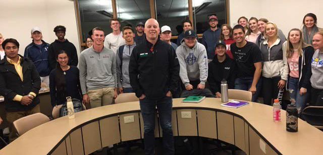 Jeff Adem poses with a group of students around a semicircle desk.