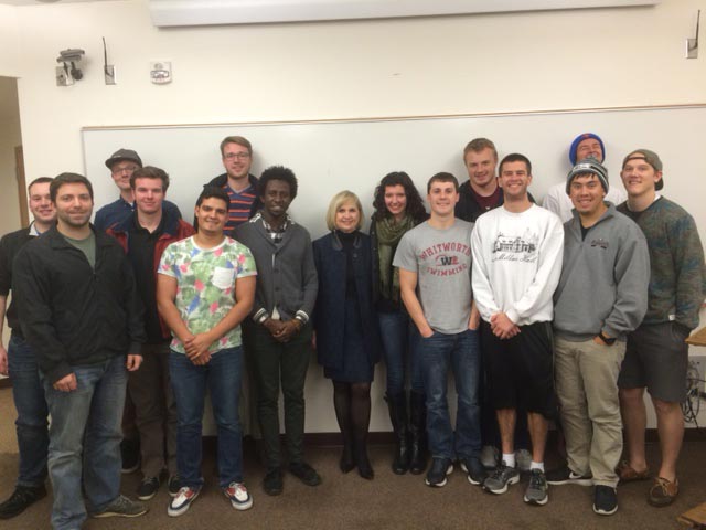 A professor and students pose, smiling, in front of a whiteboard in a classroom setting.