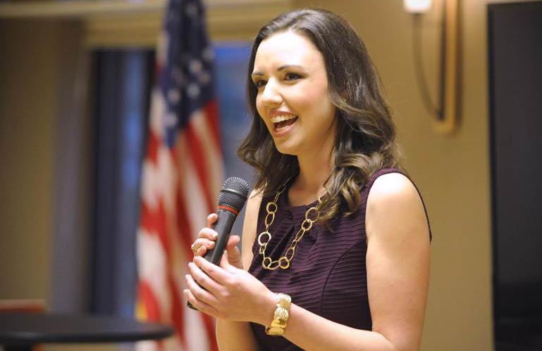 Katherine Morgan speaks into a microphone during a presentation. An American flag is in the background.