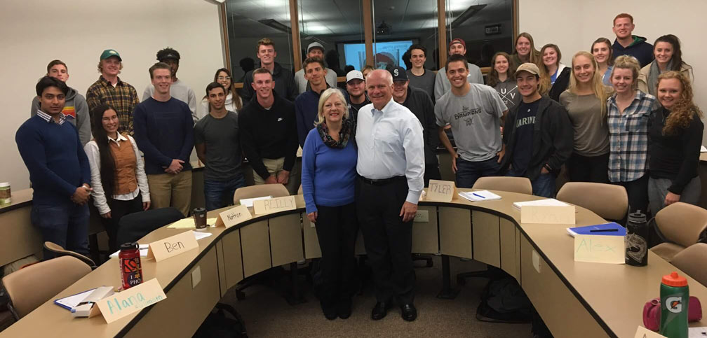 Larry Pobus and his wife pose with a group of students around a semicircle desk.
