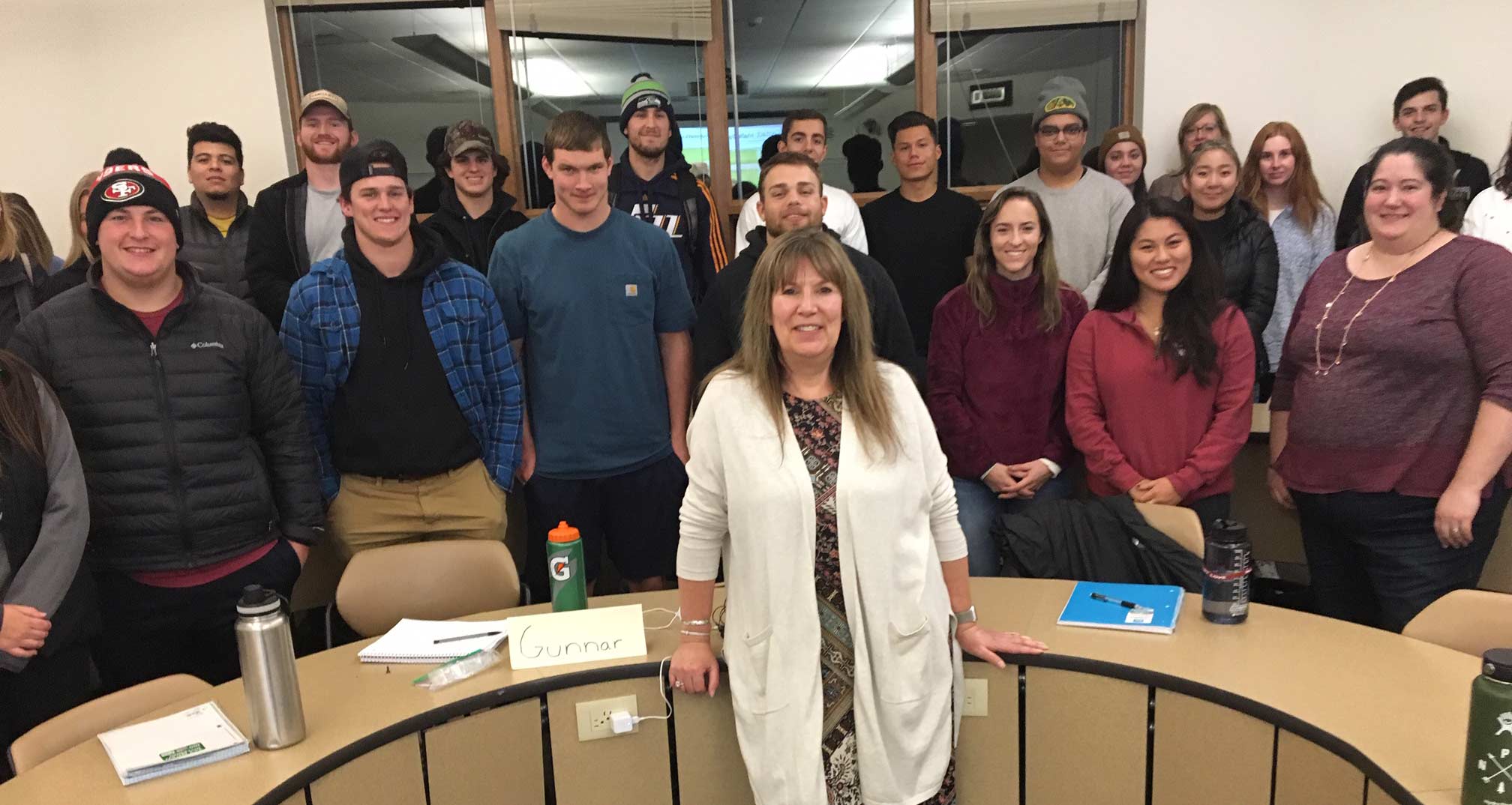 Lisa Schaffer and students pose, smiling, around a semicircle desk.