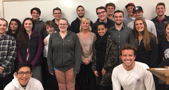 Marty Dickinson and students pose, smiling, in front of a whiteboard in a classroom setting.