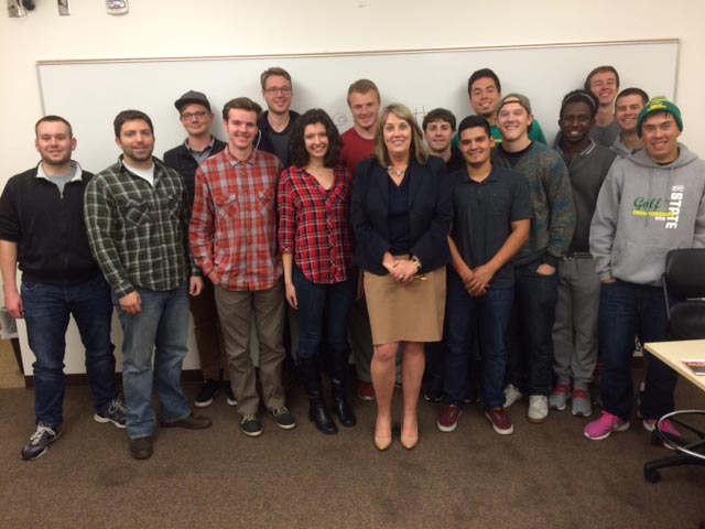 Pam Scott and students pose, smiling, in front of a whiteboard in a classroom setting.