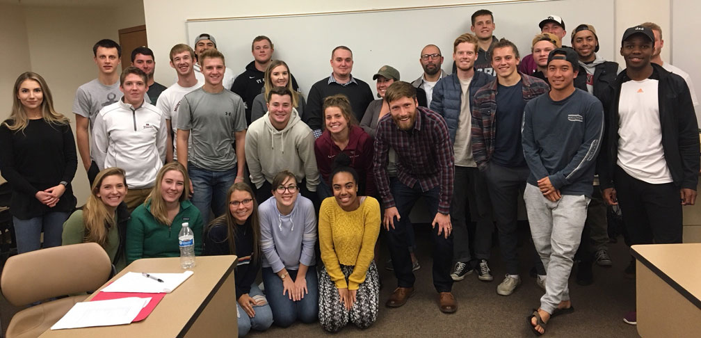 Peter Cleary and students pose, smiling, in front of a whiteboard in a classroom setting.