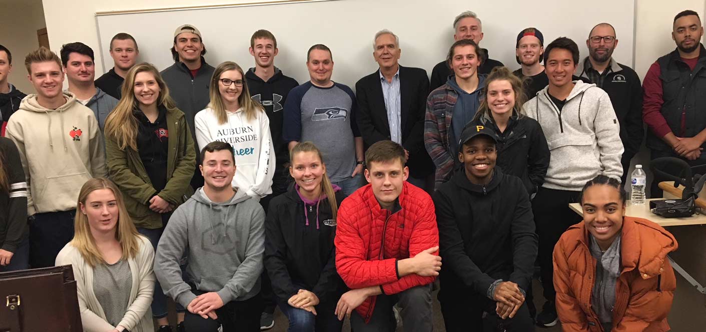 Ric Rocca and students pose, smiling, in front of a whiteboard in a classroom setting.
