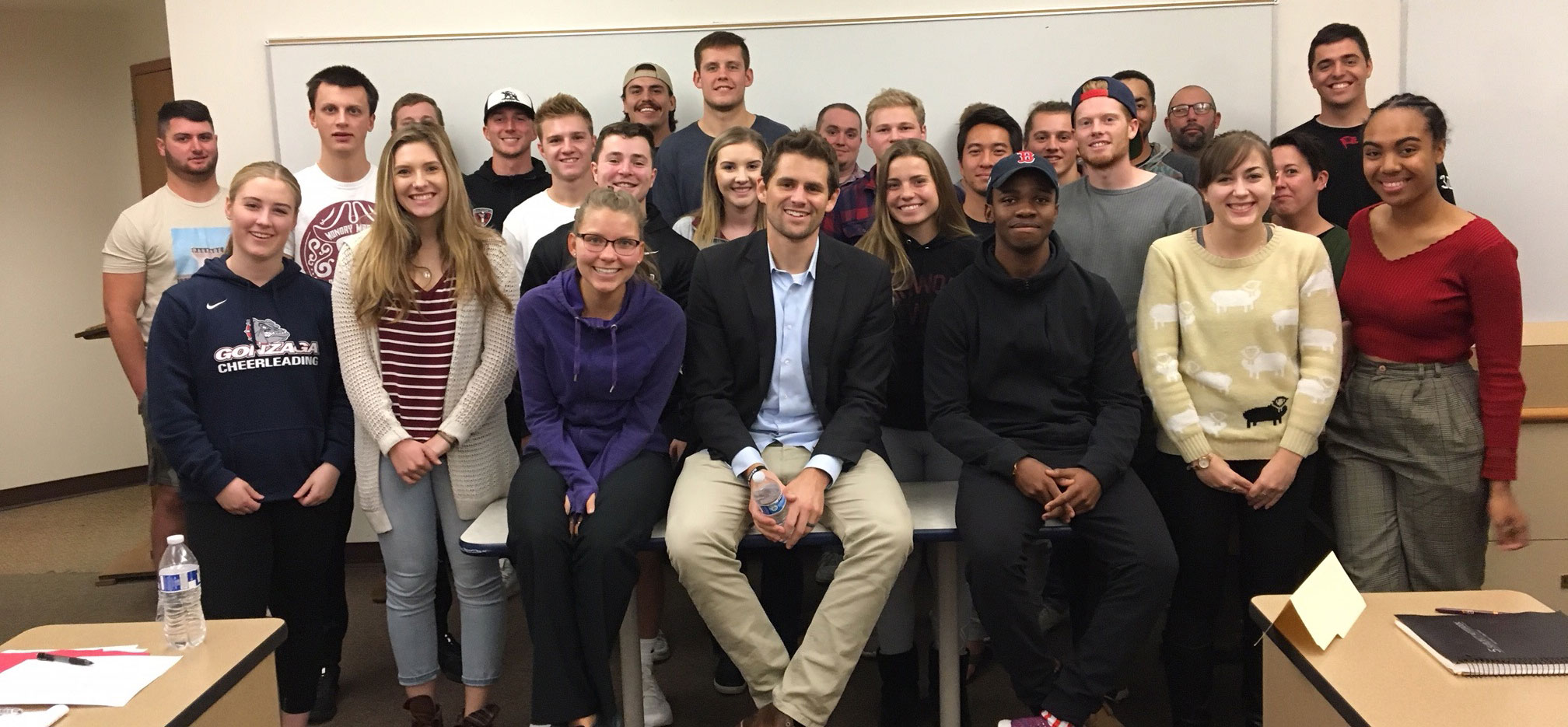 Scott Donnell and students pose, smiling, in front of a whiteboard in a classroom setting.
