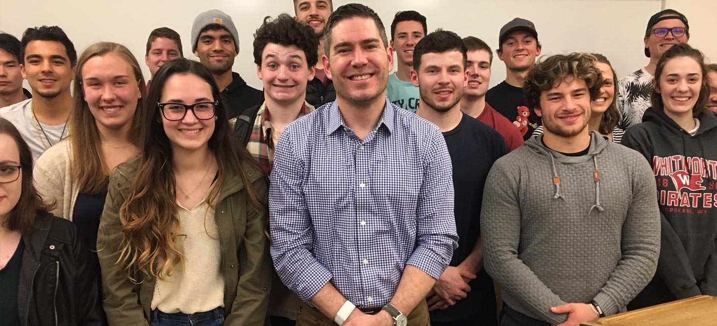 A professor and a bunch of students pose and smile broadly at the camera.