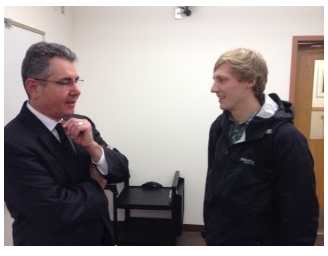 A student and professor stand in a classroom, conversing.