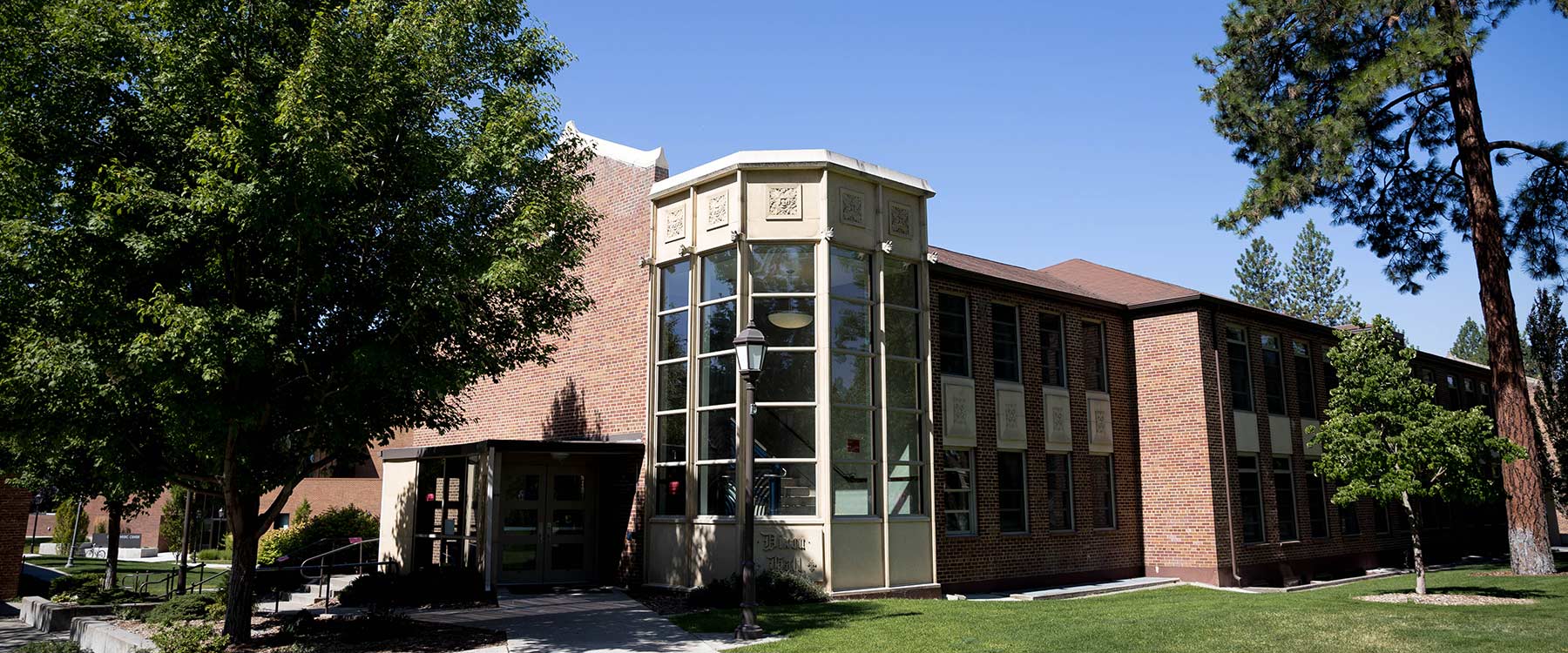 A stately, modern, brick building with classic design features, partially shaded by trees.